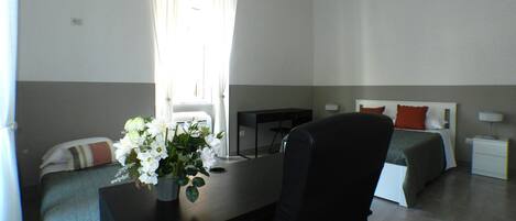 Habitación de hotel con escritorio, dos camas, una silla, lámpara de escritorio y ventana con cortinas.