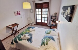 Cozy retreat with a comfortable bed, wooden chair, and bookshelf, offering a peaceful view of the outdoors.