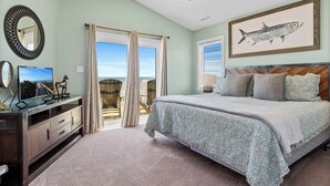 Un dormitorio con una cama, televisor, cómoda y un ventanal con cortinas.