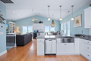 Une cuisine spacieuse avec des meubles blancs, un évier en acier inoxydable et des luminaires suspendus.