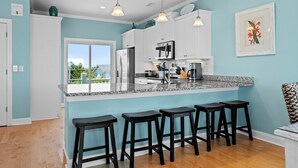 Une cuisine moderne dotée d’un grand îlot central, d’appareils électroménagers en acier inoxydable et de tabourets de bar noirs.