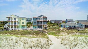 A beachfront property with multiple-story houses featuring balconies and a sandy beach in the foreground. - Luxury Oceanfront Home: Private Pool, Elevator Access, Game Room & More! (Emerald Isle)