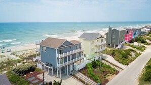 A beachfront property with multiple-story houses, a visible beach, and a road leading to the beach. - Luxury Oceanfront Home: Private Pool, Elevator Access, Game Room & More! (Emerald Isle)
