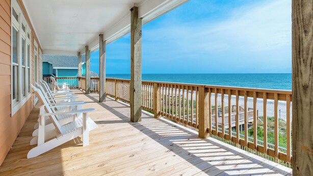 A wooden deck with white chairs, a wooden railing, and a view of the ocean. - Oceanfront 8 Bedroom/6.5 Bath Home: Elevator, Gourmet Kitchen, Pool, Hot Tub, St (Emerald Isle)