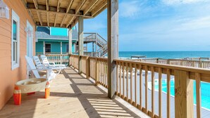 A wooden deck with a view of the ocean, a pool, and a building with a turquoise roof. - Oceanfront 8 Bedroom/6.5 Bath Home: Elevator, Gourmet Kitchen, Pool, Hot Tub, St (Emerald Isle)