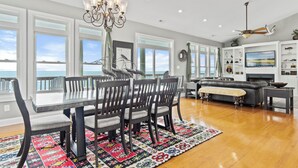 A spacious living room with a dining area, large windows, a fireplace, and a view of the ocean. - Oceanfront 8 Bedroom/6.5 Bath Home: Elevator, Gourmet Kitchen, Pool, Hot Tub, St (Emerald Isle)