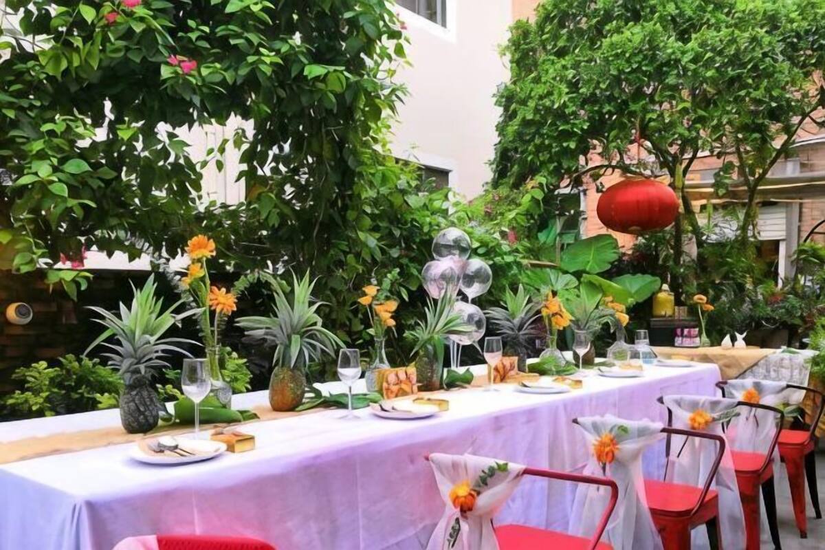 Un área de comedor al aire libre con una mesa dispuesta para una comida, rodeada de follaje y plantas.