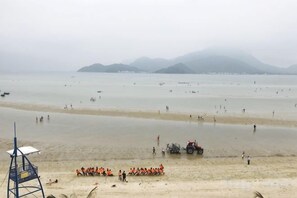 Una playa con una torre de salvavidas, gente con chalecos anaranjados y un tractor sobre la arena.