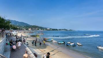 Escena de playa costera con gente, barcos y un jet ski.