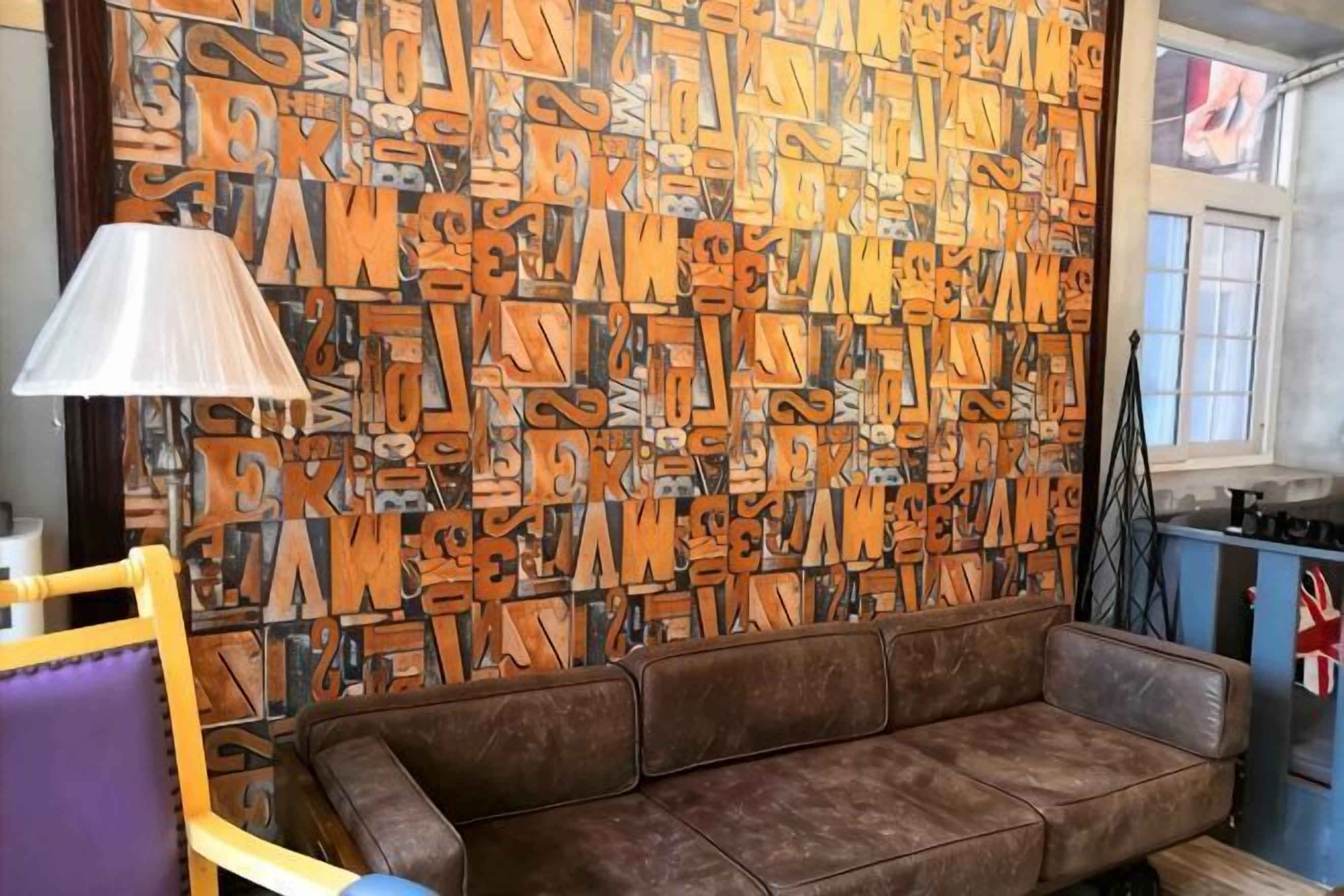 Une pièce avec un mur orné de motifs, un canapé marron, une lampe et une fenêtre donnant sur un paysage.