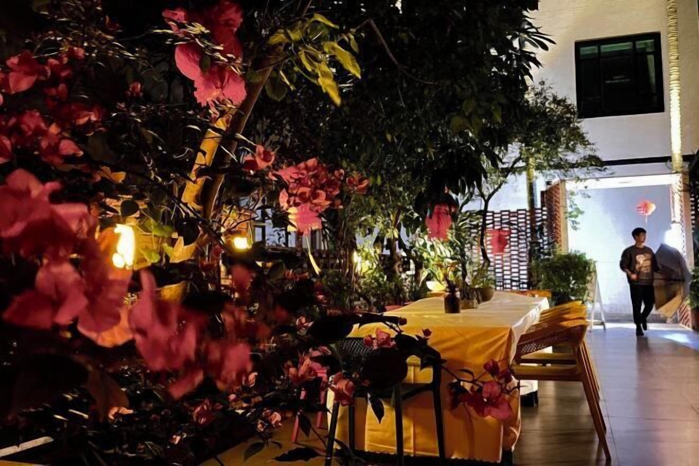 An outdoor dining area with a yellow tablecloth, surrounded by potted plants and flowers.