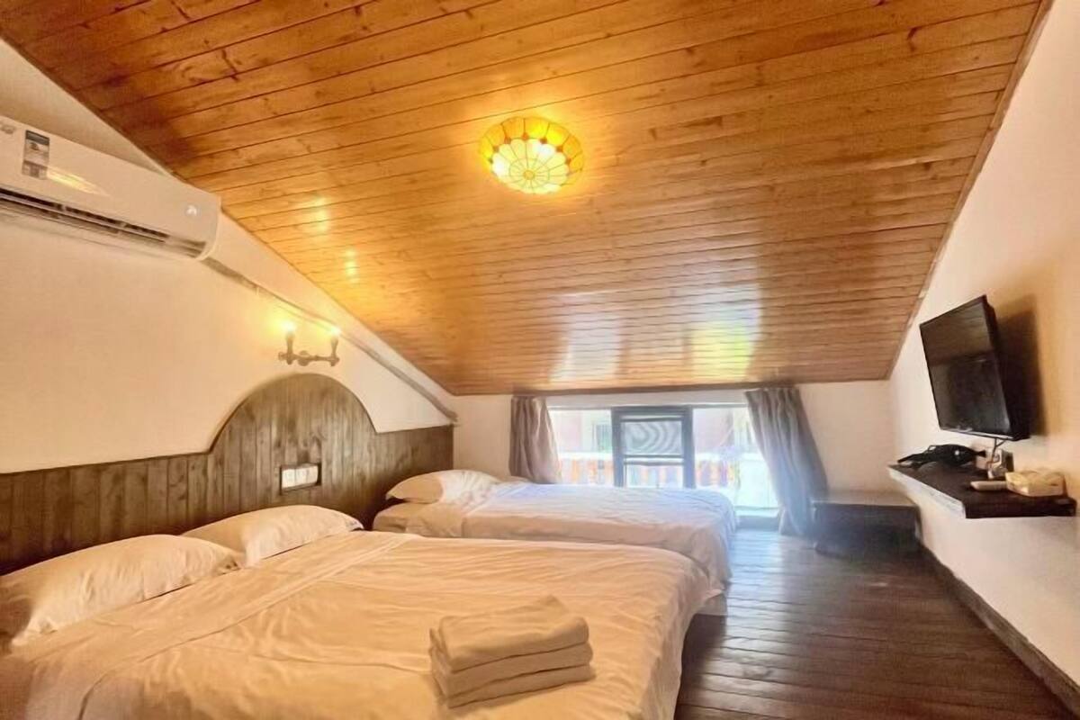 Habitación de hotel con dos camas, techo de madera, aire acondicionado, televisor y una ventana con cortinas.