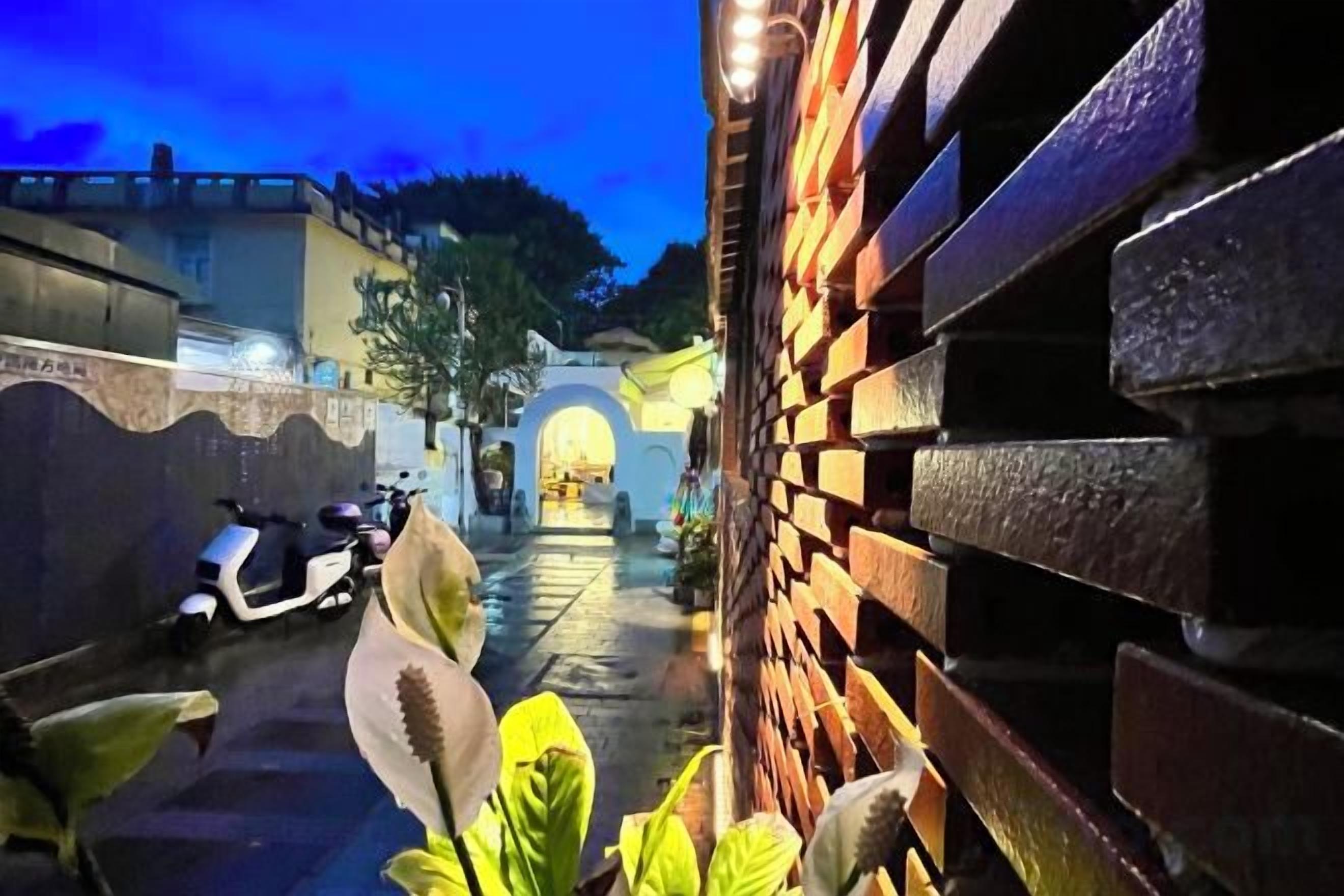 Un callejón estrecho con un muro de ladrillo a un lado y una moto estacionada al otro.