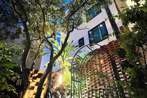 Un patio con muro de ladrillo, una reja metálica y árboles.