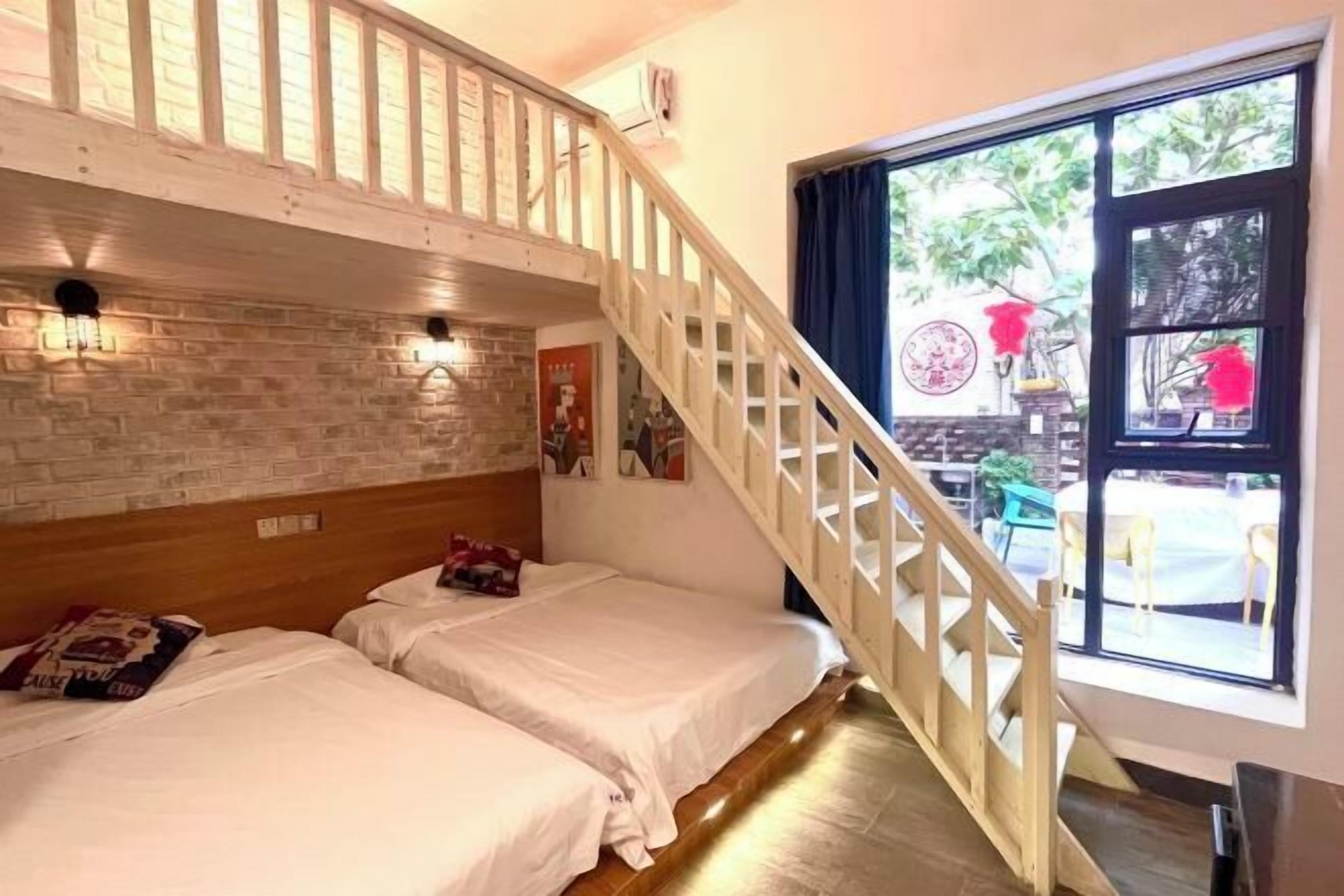 Una habitación con dos camas, una escalera de madera y un ventanal con vistas al exterior.