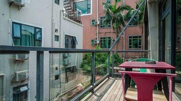 A balcony with a red table, glass railings, and a view of a brick building with multiple windows and air conditioning units.