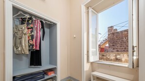 A room with a wardrobe, a bench, and a window with a view of a brick wall and power lines. - Art Room n3 (Meta)