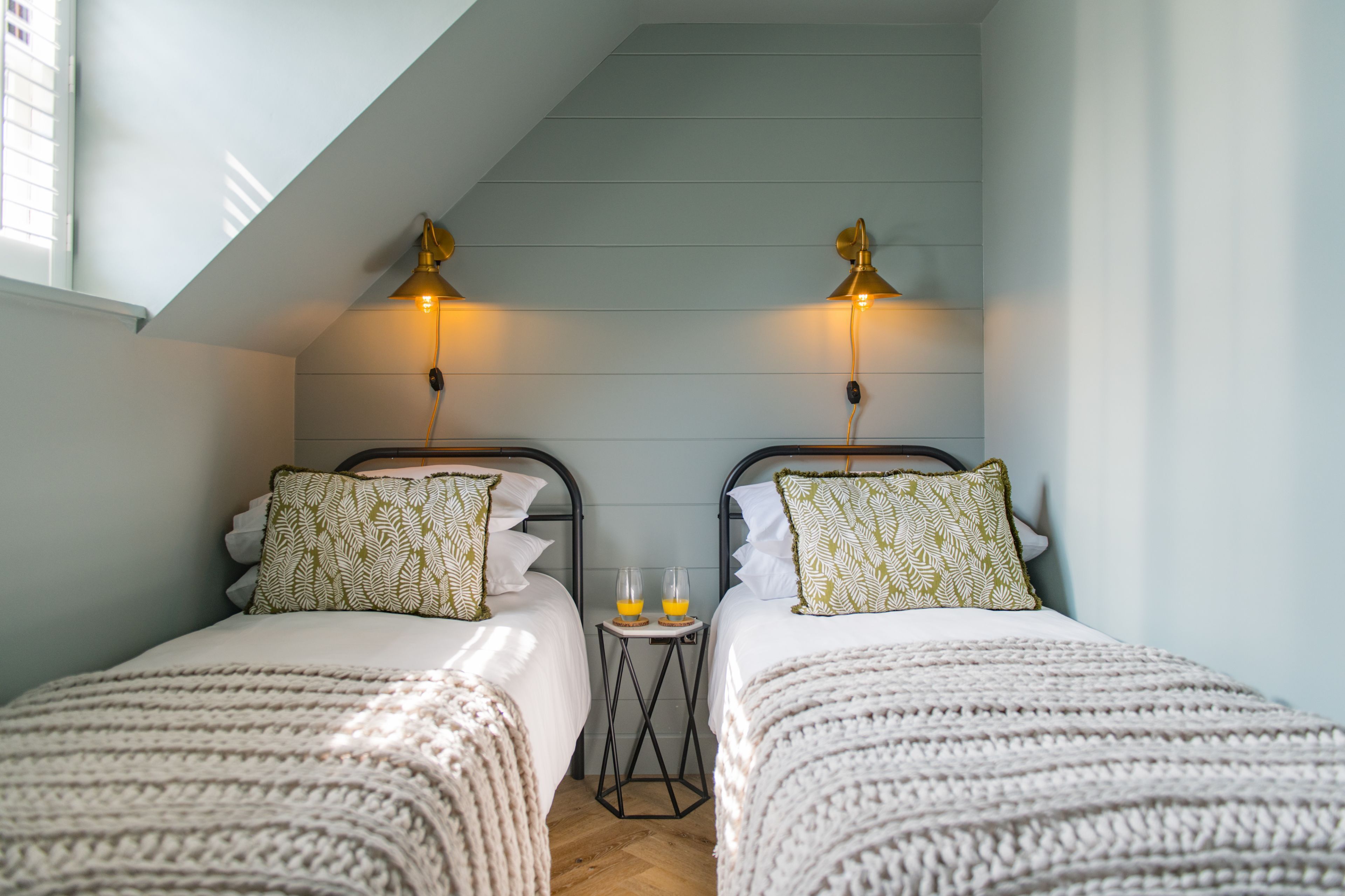 A bedroom with two beds, a small table with two glasses of orange juice, and two wall-mounted lamps.
