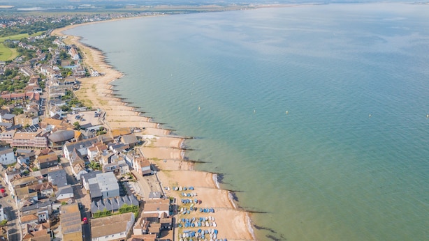 Luchtbeeld van een kustplaatsje met een strand, huizen en boten.