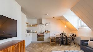 Een moderne keuken met witte kasten, een grote televisie en een eethoek met een houten tafel en stoelen.