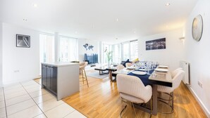 Een ruime woonkamer met een eettafel voor zes personen, een keuken en grote ramen voor natuurlijk licht.