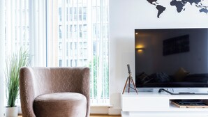 Een moderne woonkamer met een grote flatscreen televisie, een gestreept fauteuil, een potplant en een wereldkaart aan de muur.
