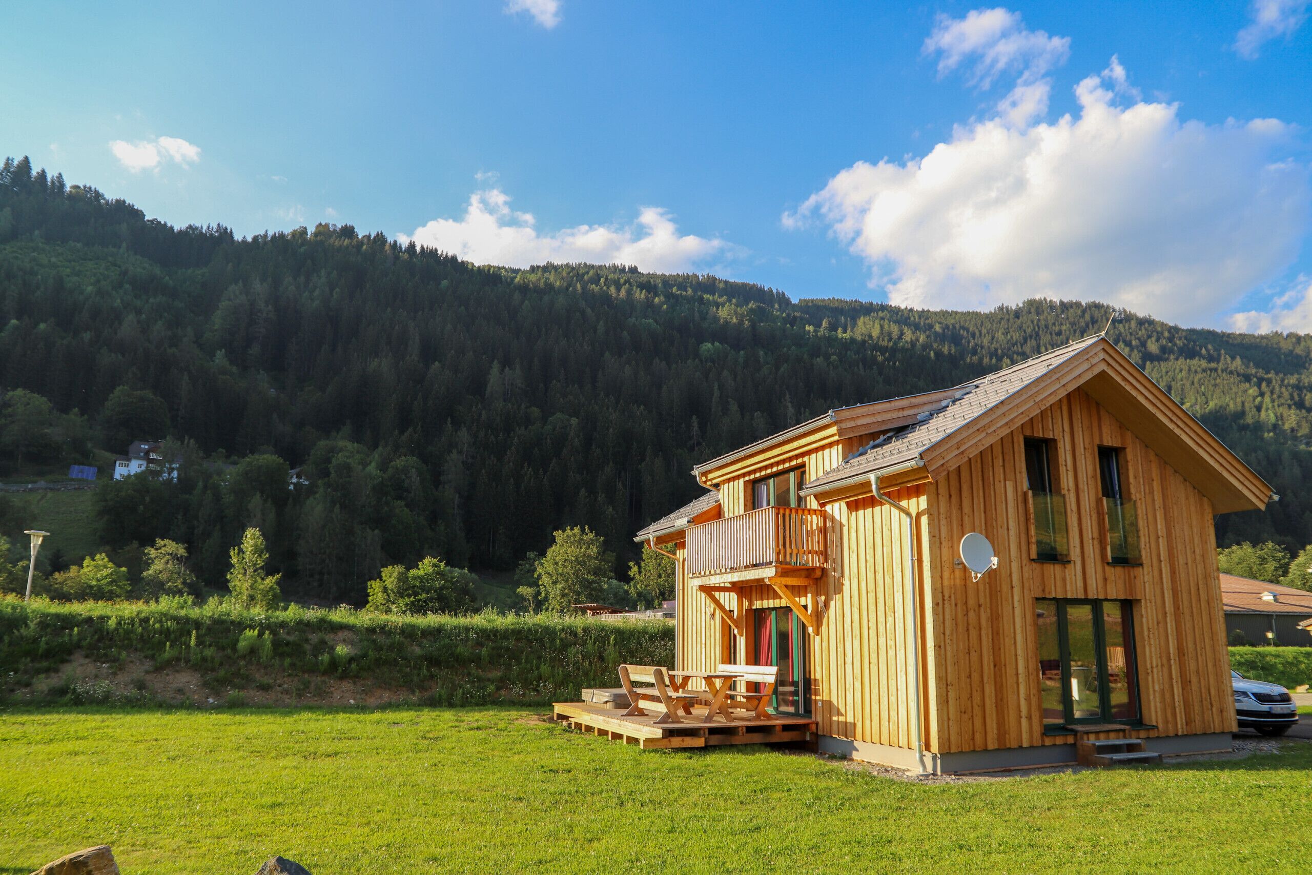 A wooden cabin with a balcony, a deck, and a view of a forested mountain.