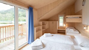 A wooden cabin with three beds, a sliding glass door to a balcony, and a small kitchen area. - Murau 5 - Chalet Murlaub (Murau)
