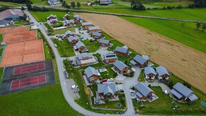 An aerial view of a residential area with multiple wooden houses, a tennis court, and a large field. - Murau 13 - Chalet Murau (Murau)