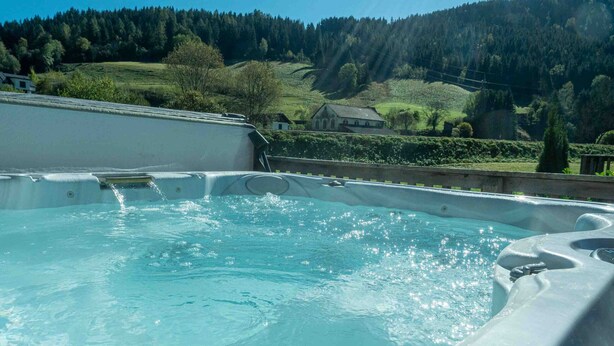 A hot tub with a clear view of a forested hillside and a house in the background. - Murau 13 - Chalet Murau (Murau)