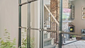 A staircase with a brick column, a living room with a sofa and a TV, and a white rug. - Historic 4th and Gill Charmer (Mid-Term Available) (Knoxville)