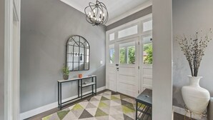 A hallway with a geometric patterned rug, a console table with a mirror, a vase with dried flowers, and a chandelier. - Historic 4th and Gill Charmer (Mid-Term Available) (Knoxville)