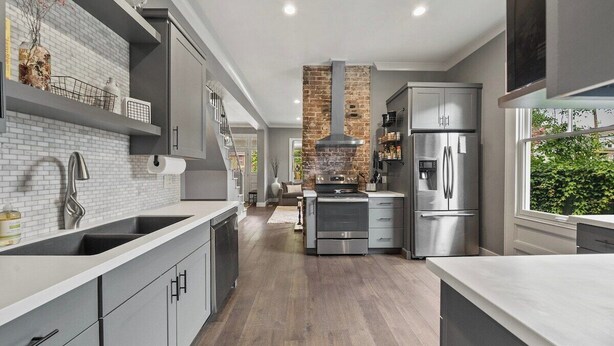 A modern kitchen with grey cabinetry, a brick accent wall, stainless steel appliances, and a view of the outdoors. - Historic 4th and Gill Charmer (Mid-Term Available) (Knoxville)