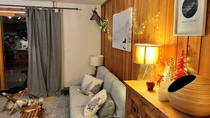 A cozy living room with a grey sofa, a wooden side table, a lamp, and a deer head mounted on the wall. - Appartement Privé Dans Chalet Proche des Cimes, Départ et Retour ski aux Pieds (Montgenèvre)