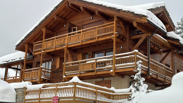 A wooden chalet with multiple balconies, stone foundation, and a sign indicating a private parking area. - Appartement Privé Dans Chalet Proche des Cimes, Départ et Retour ski aux Pieds (Montgenèvre)