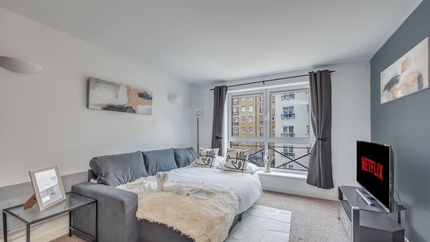 A modern bedroom with a bed, grey sofa, and a TV displaying 'NETFLIX'. - Elegant Apartment in City Centre • Fast Wifi • Smart TV • Access to Communal Gym (Northampton)