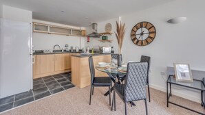 A modern kitchen with a central island, a dining area with a glass table and black chairs, and a large wall clock. - Elegant Apartment in City Centre • Fast Wifi • Smart TV • Access to Communal Gym (Northampton)
