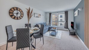 A modern living room with a dining area, a large wall clock, and a sofa. - Elegant Apartment in City Centre • Fast Wifi • Smart TV • Access to Communal Gym (Northampton)