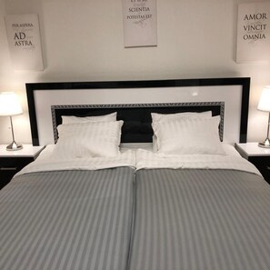 A neatly made bed with striped bedding, two bedside lamps, and framed text on the wall.