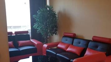 Una sala de estar moderna con sofás rojos y negros, una mesa redonda de centro y una planta grande en maceta.