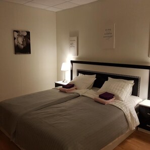 A double bed with a black headboard, two bedside tables with lamps, and a wall with a framed picture and two signs. - Skinnargården (Malung)