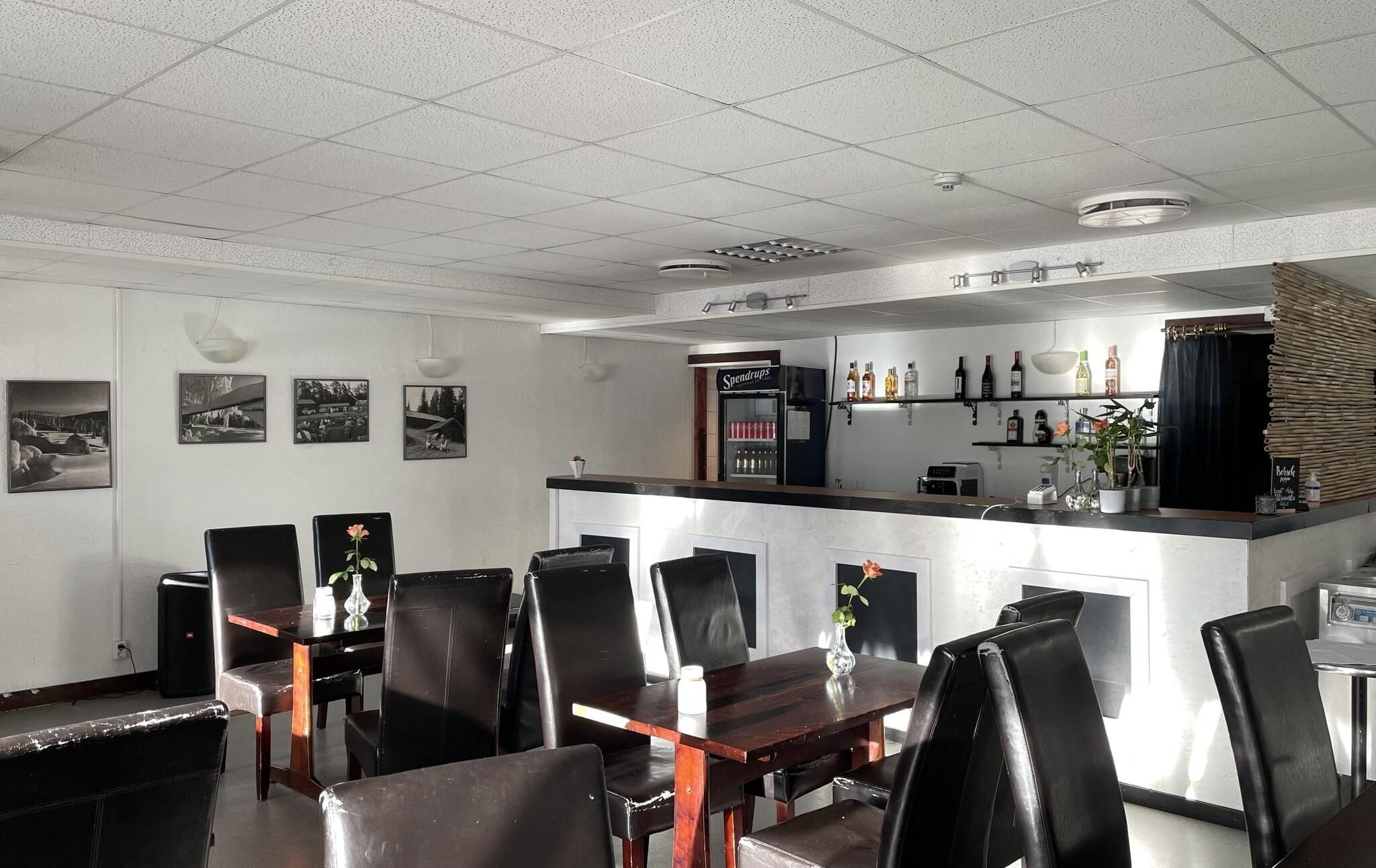 Un restaurante con zona de bar, sillas de cuero negro y un refrigerador lleno de bebidas.