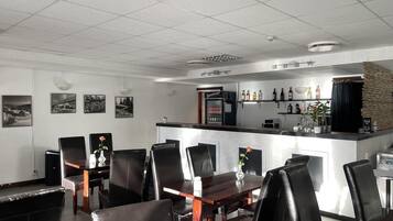 Un restaurante con zona de bar, sillas de cuero negro y un refrigerador lleno de bebidas.