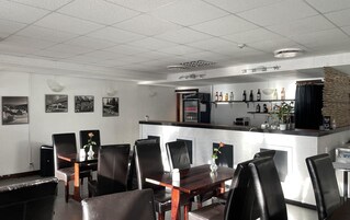 Un restaurante con zona de bar, sillas de cuero negro y un refrigerador lleno de bebidas.