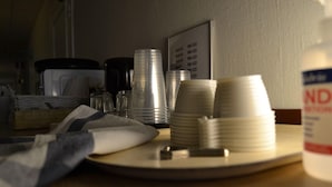 Una mesa con pilas de platos blancos y cubiertos, un dispensador de gel antibacterial y un panel con el menú de fondo.