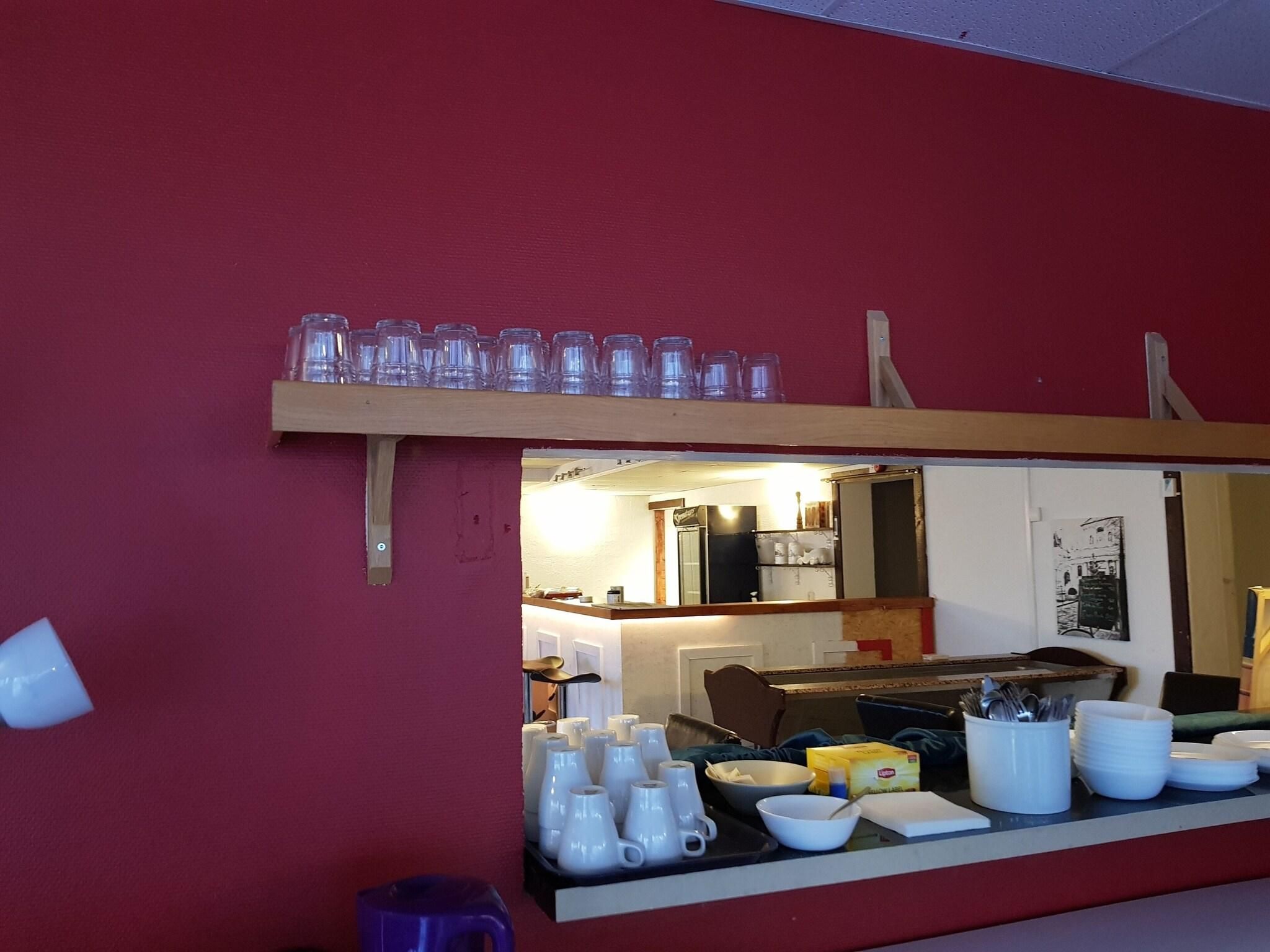 Eine Küche mit roter Wand, einem Holzregal mit Tassen sowie einer Arbeitsplatte mit Schüsseln und Besteck.