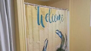 A bathroom with a yellow shower curtain featuring a welcome message and a sea turtle illustration.