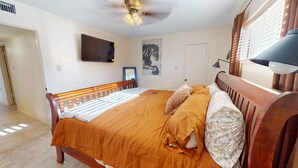 A bedroom with a wooden bed, a ceiling fan, a mounted TV, and a door. - NEW LISTING Right At Home-Midland Cowboy Siesta Corner Lot w/ Patio & Cov'd Park (Midland)