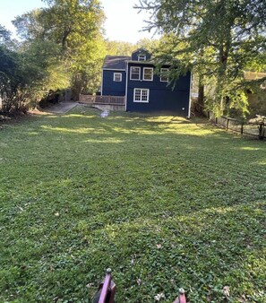 A house with a dark exterior, a grassy yard, and a wooden deck. - Atlanta-Themed Home, Sleeps 7, 10 Min to Stadium & Downtown (East Point)