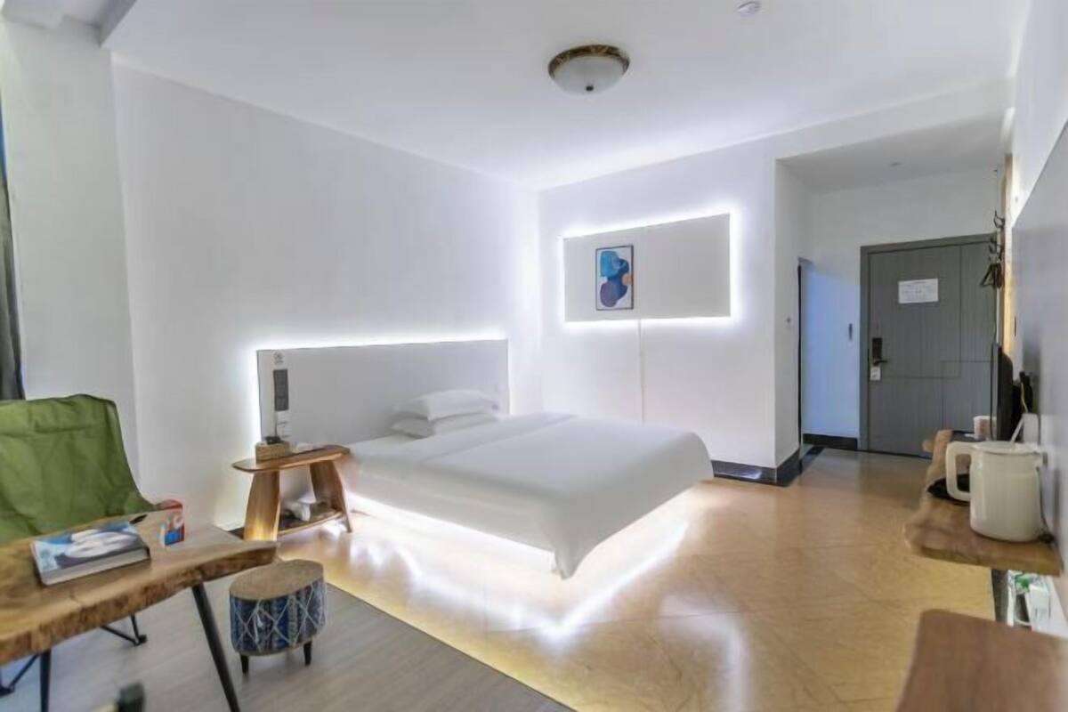 A modern hotel room with a bed, bedside table, lamp, and a green chair.